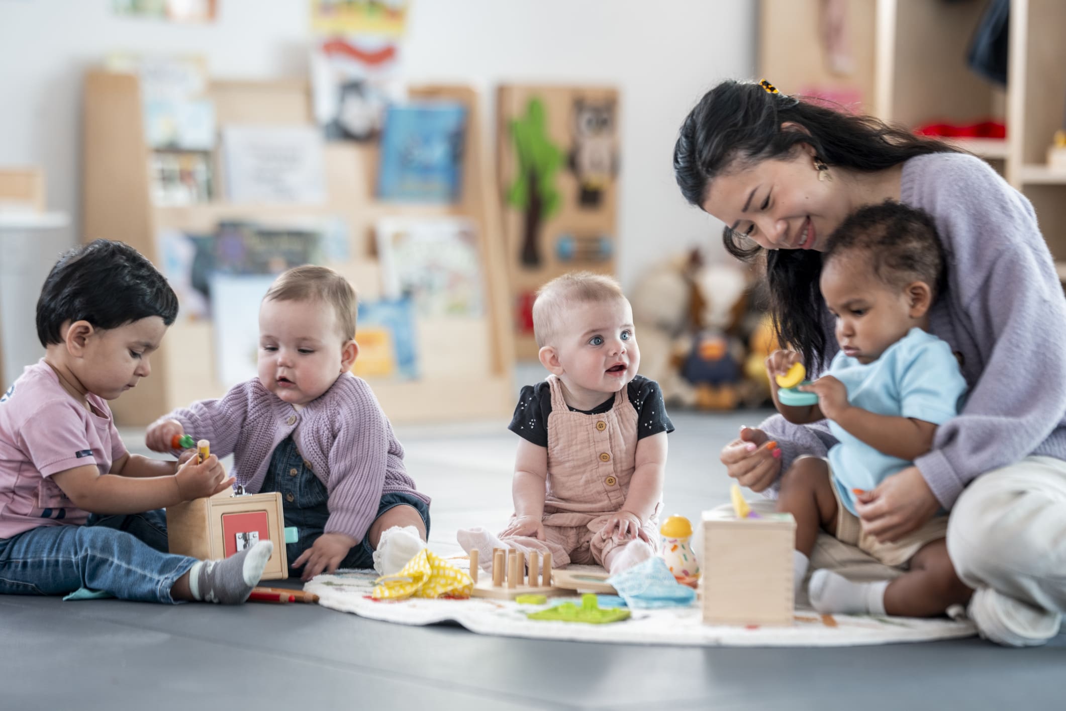 Smiling Caregiver Playing With Diverse Group Of Toddlers in Bright Nursery - Maryvale